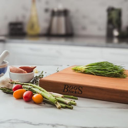 Wooden cutting board with 'Boos Blocks' branding on a kitchen counter with vegetables.