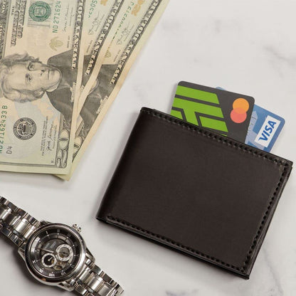 Black wallet with cards, dollar bills, and a watch on a light surface