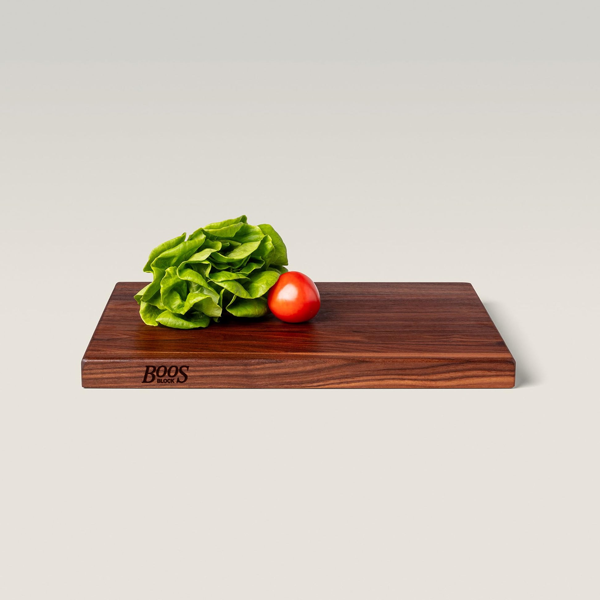 Wooden cutting board with a tomato and lettuce on a light gray background