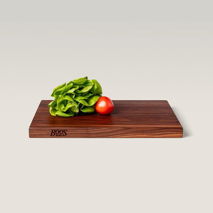 Wooden cutting board with a tomato and lettuce on a light gray background