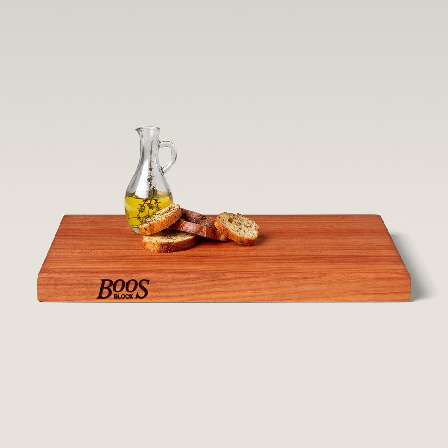 Wooden cutting board with bread slices and a carafe of oil on a light background