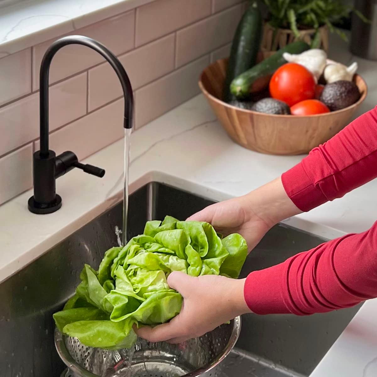 Person washing lettuce under running water in a kitchen sink with vegetables in the background.