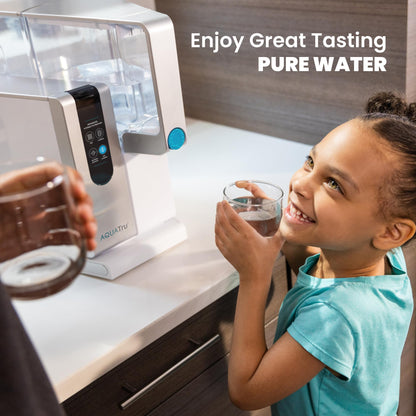 Child drinking water from a glass next to an AQUATru water filtration system.