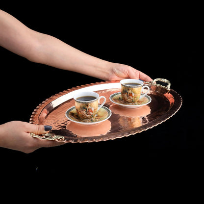 Ceramic cups with saucers on a decorative tray held by hands against a black background