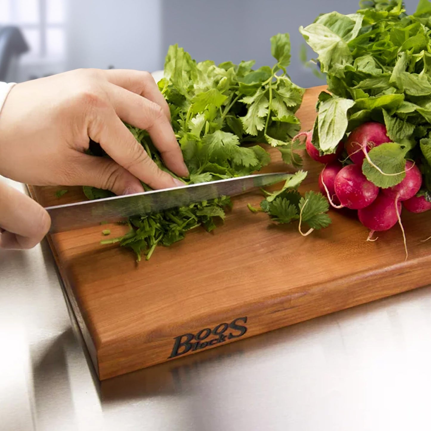 Person cutting greens on a wooden cutting board with 'Boos Block' branding