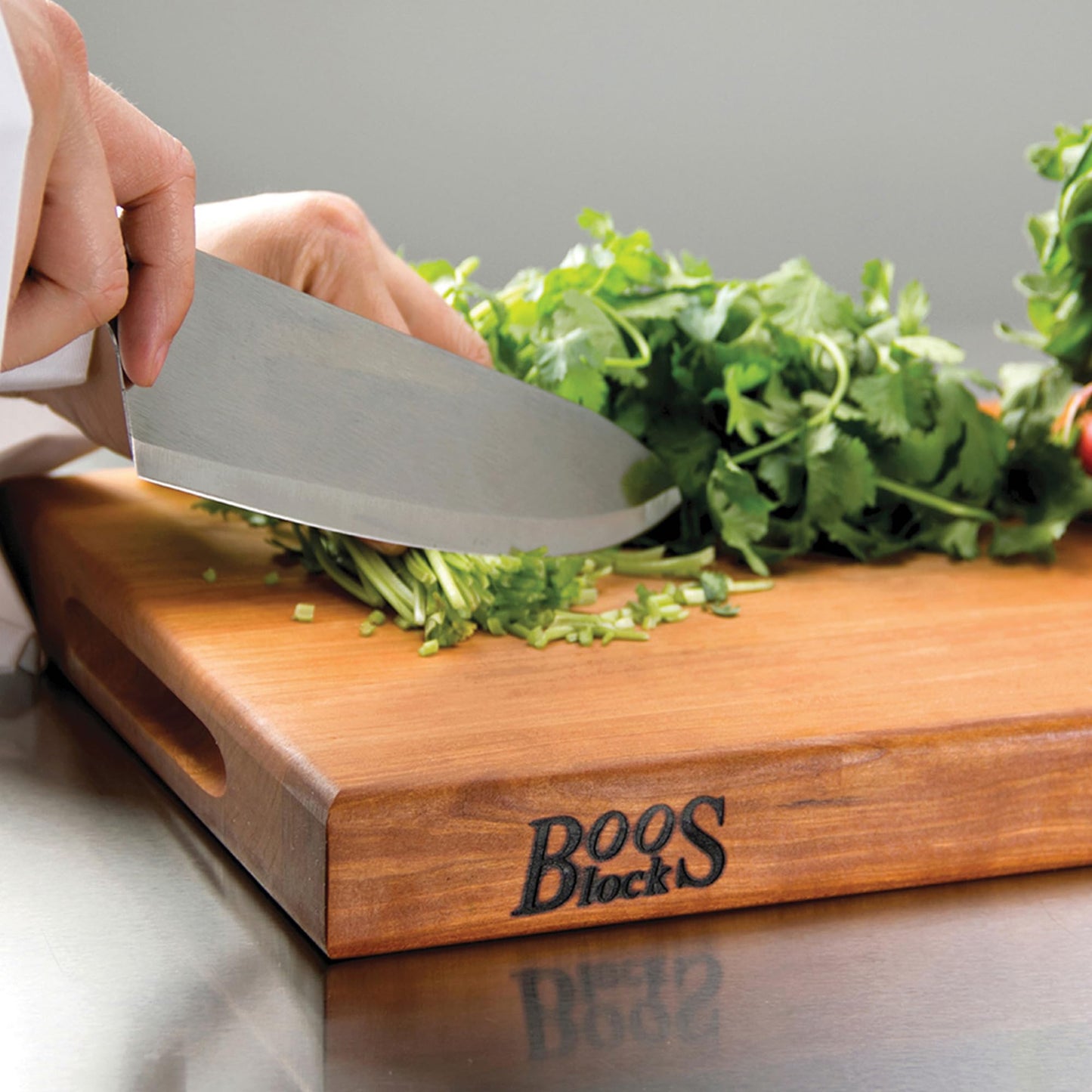 Person using a knife to chop greens on a wooden cutting board with 'Boos Block' branding.