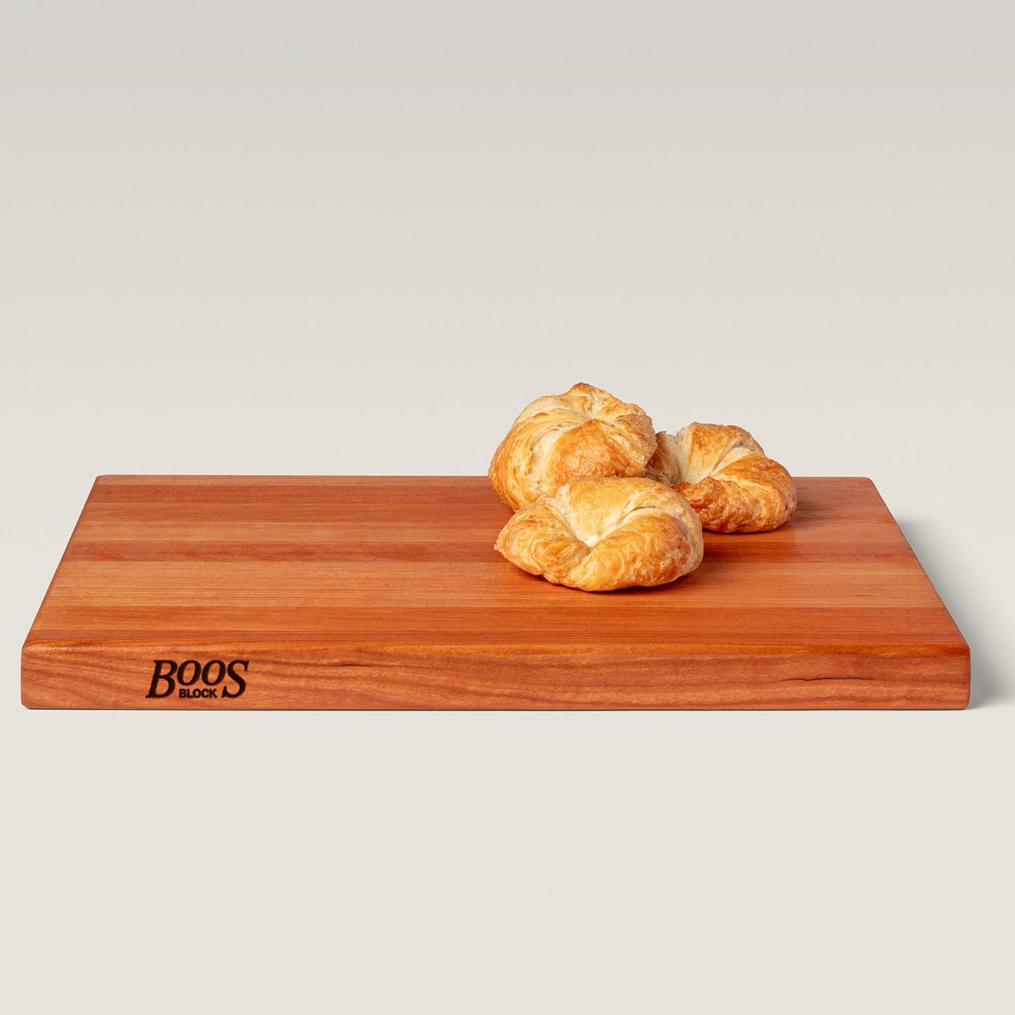 Wooden cutting board with 'BOOS Block' branding and croissants on a light gray background