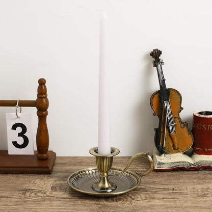 Decorative setup with a candle in a brass holder, violin model, and music-themed book on a wooden surface.