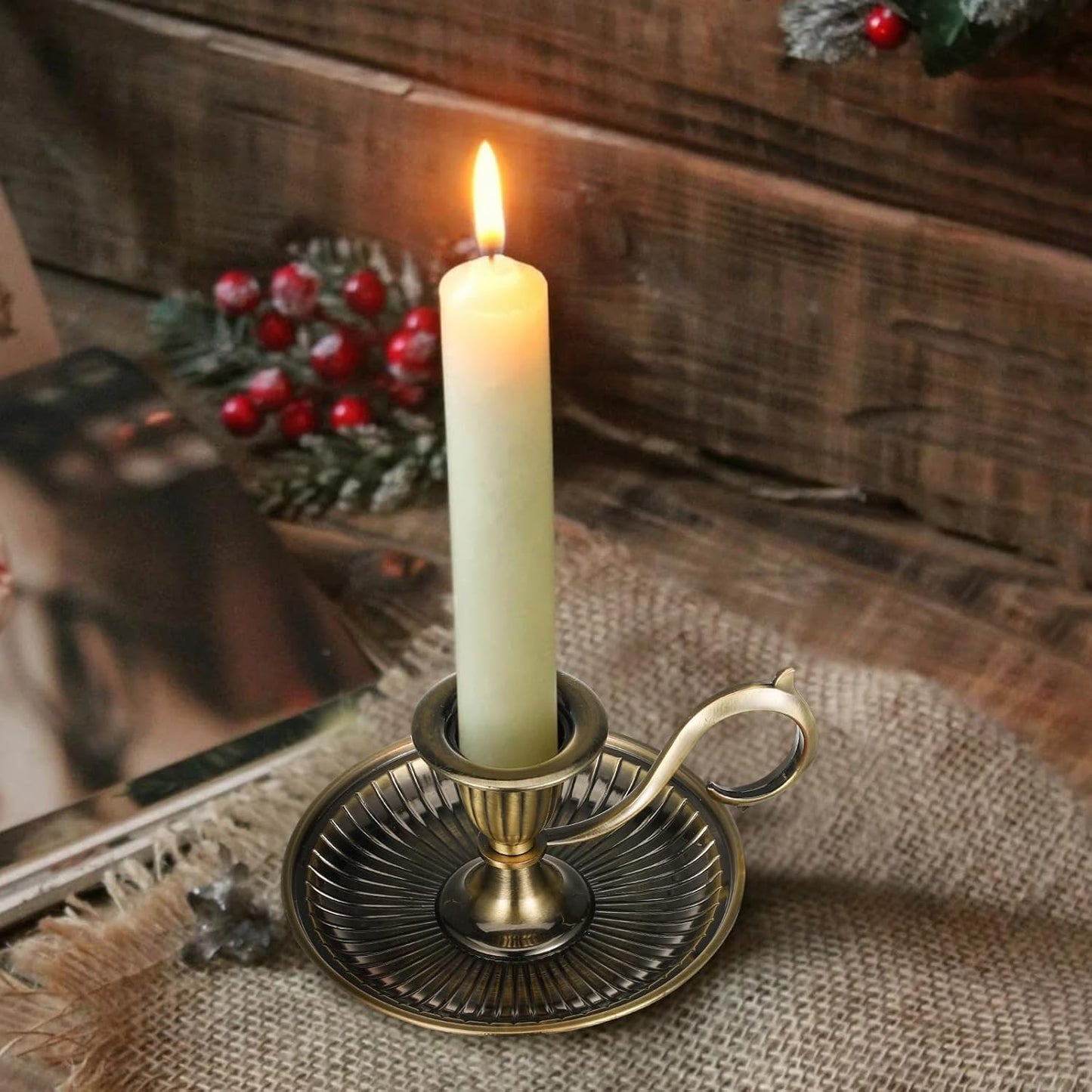 Candle in a decorative holder on a rustic wooden surface with a mirror and Christmas decorations.