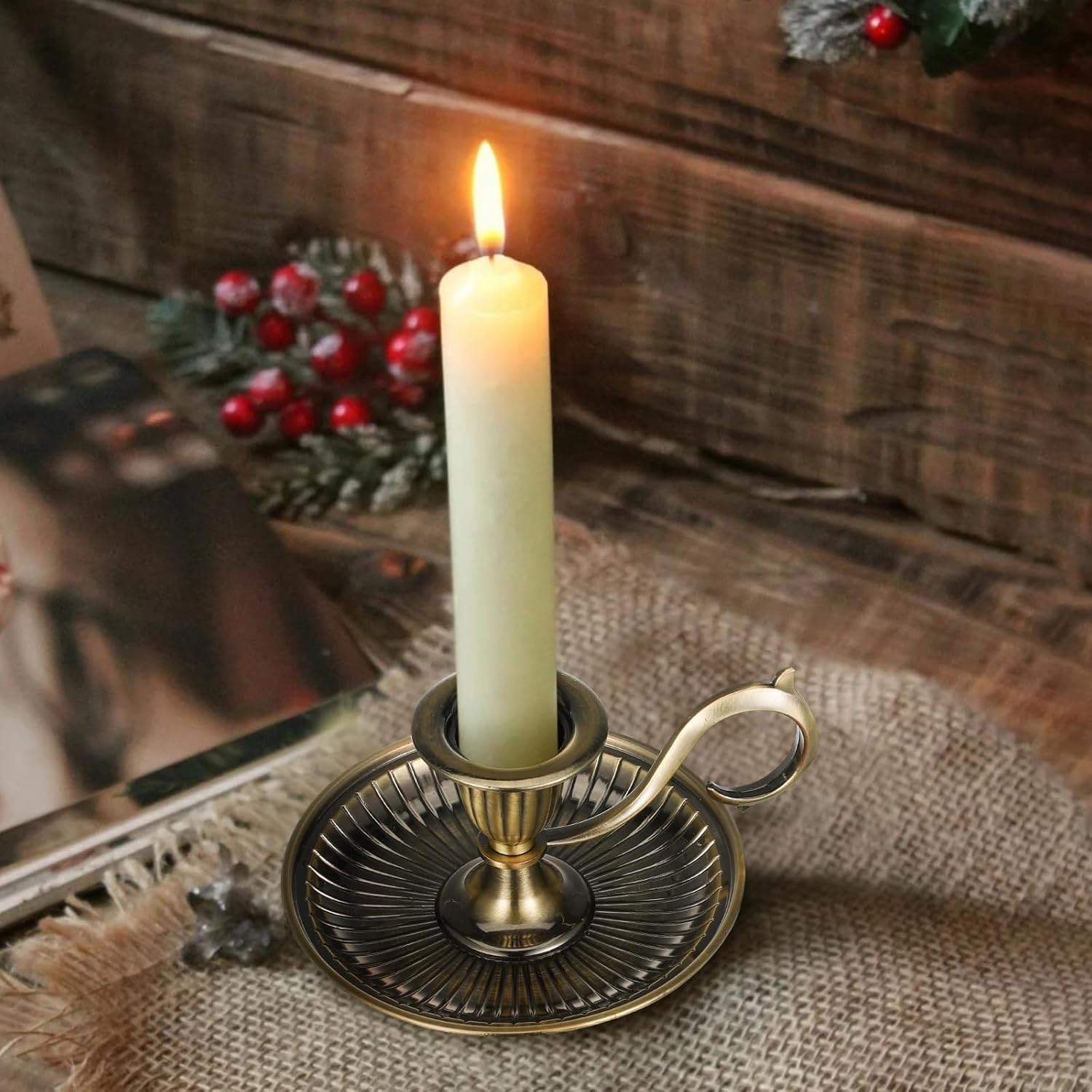Candle in a decorative holder on a rustic wooden surface with a mirror and Christmas decorations.