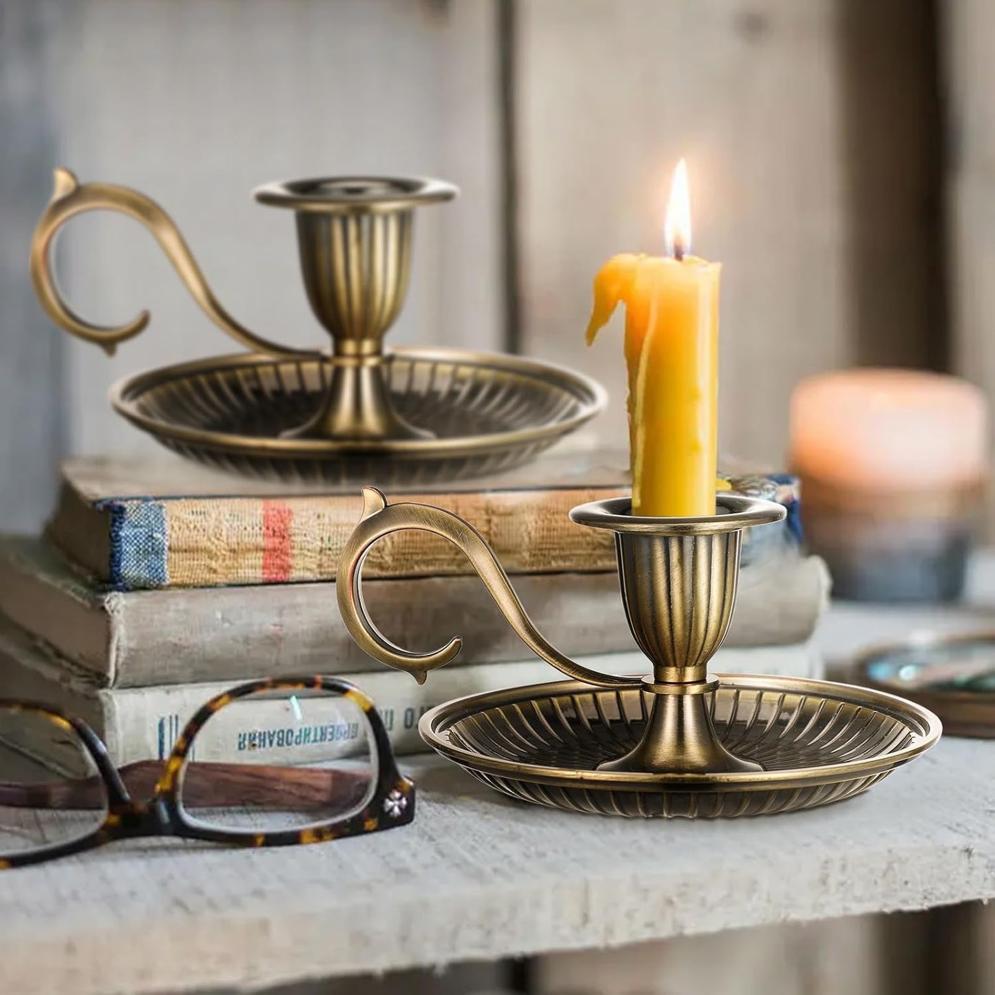 Bronze candle holder with a lit candle on a surface with books and glasses.