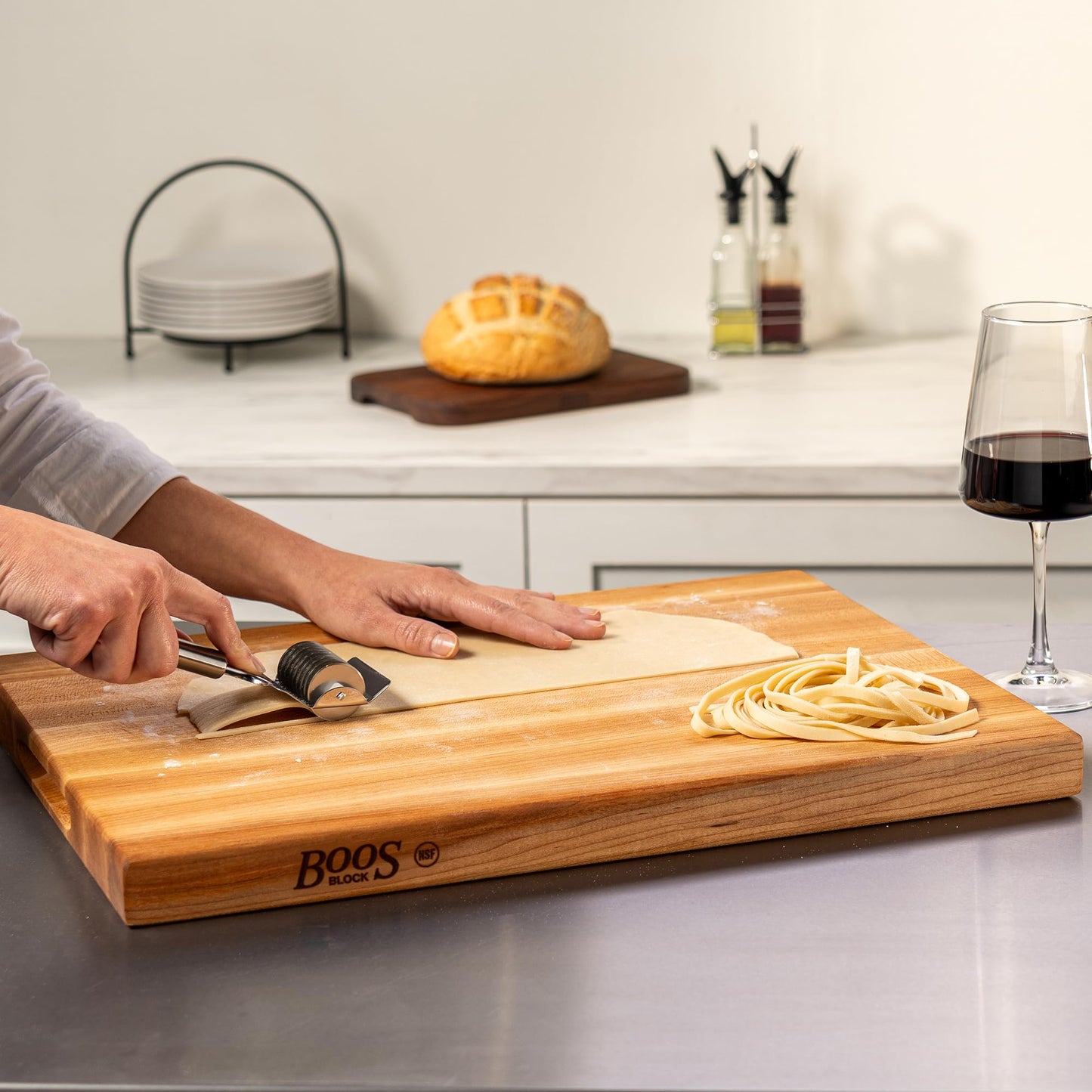 Person using a knife on a wooden cutting board with 'BOOS' branding in a kitchen setting.