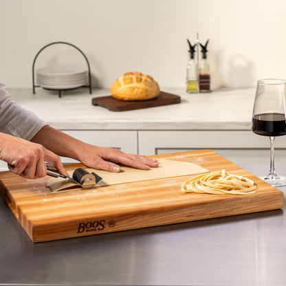 Person using a knife on a wooden cutting board with 'BOOS' branding in a kitchen setting.