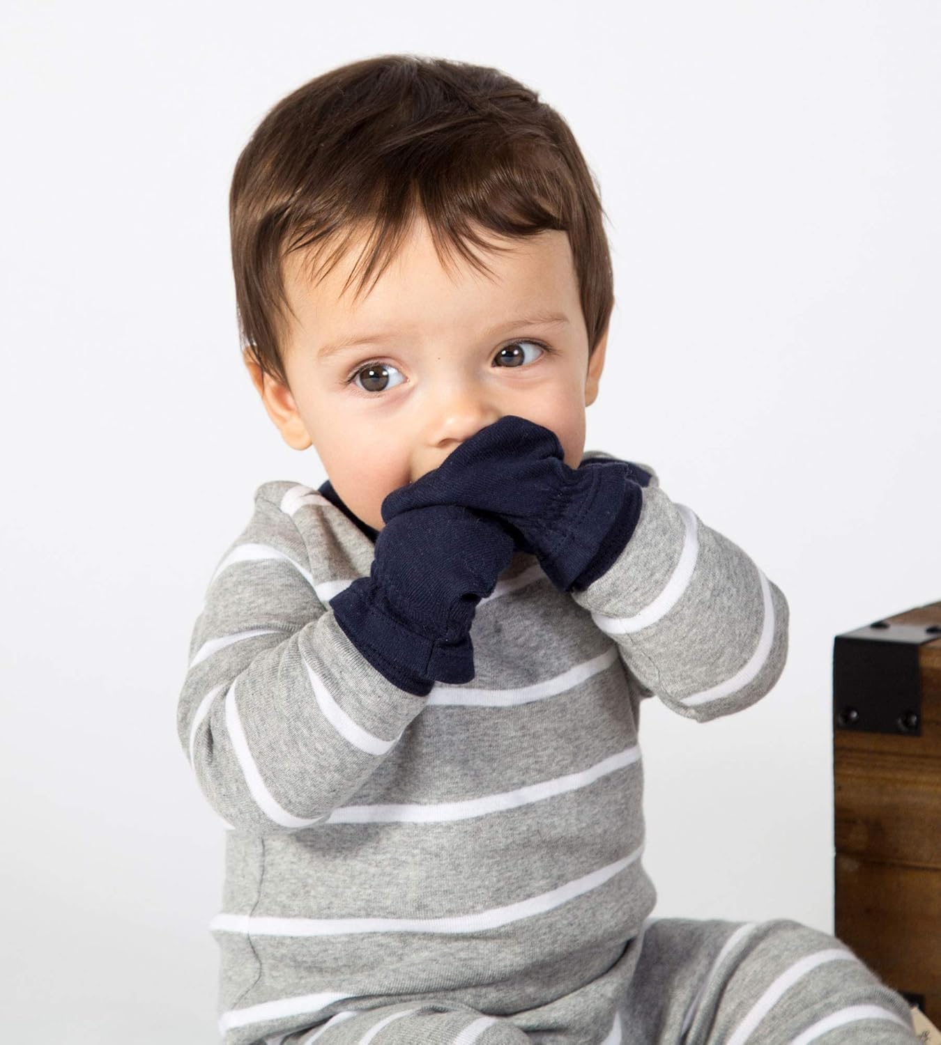 Child wearing a gray and white striped outfit with navy gloves on a plain background