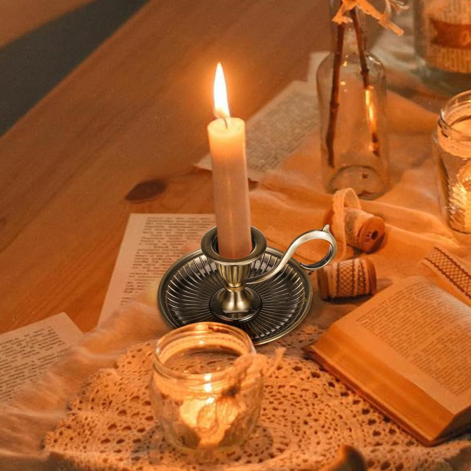 Candle in a holder on a wooden table with books and jars
