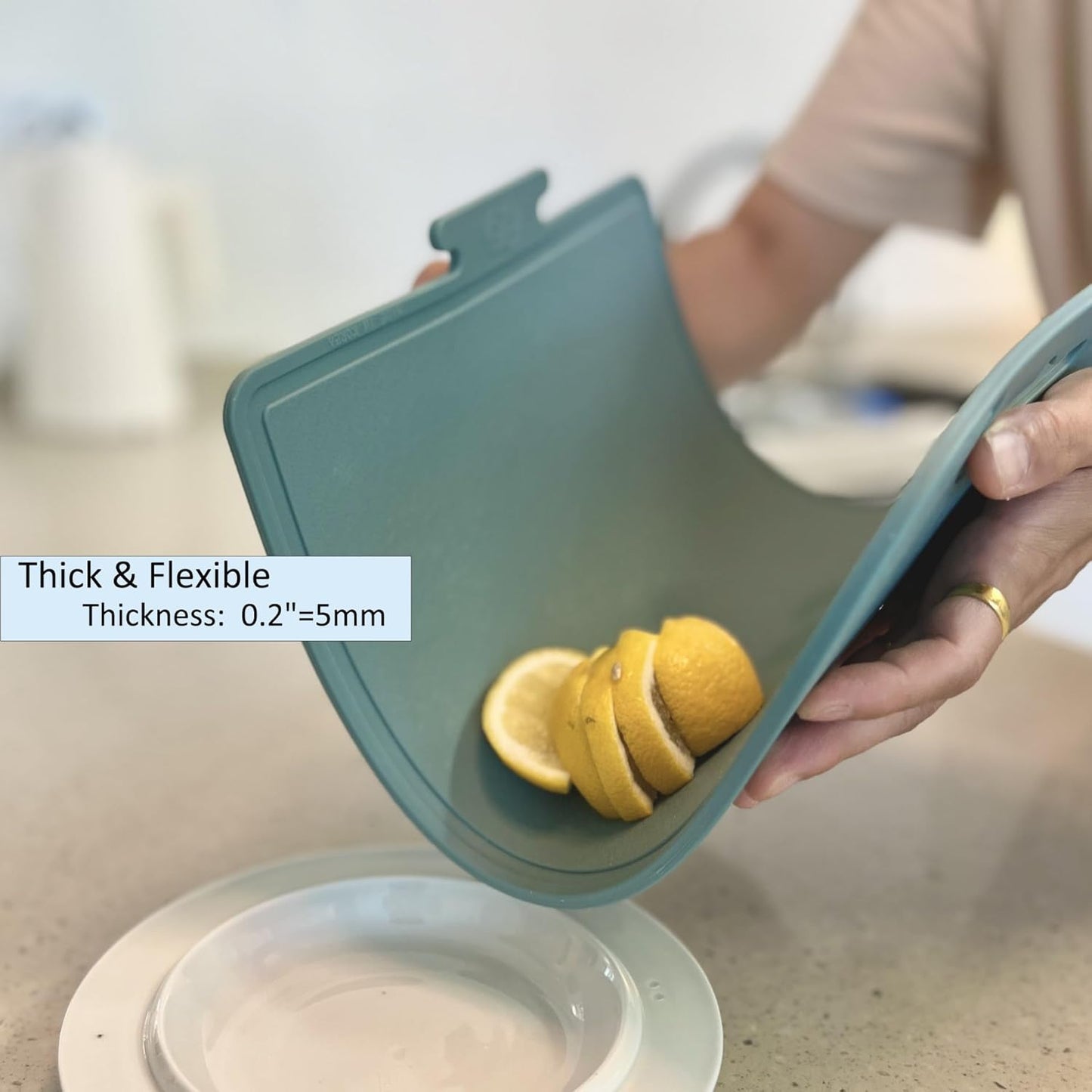 Person holding a teal silicone cutting board with sliced lemons on a kitchen counter