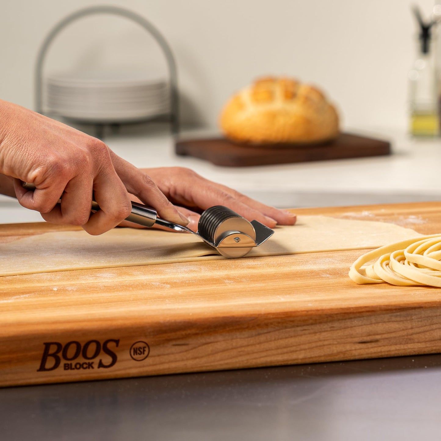 Person using a pasta cutter on dough on a wooden board with 'Boos Block' branding.