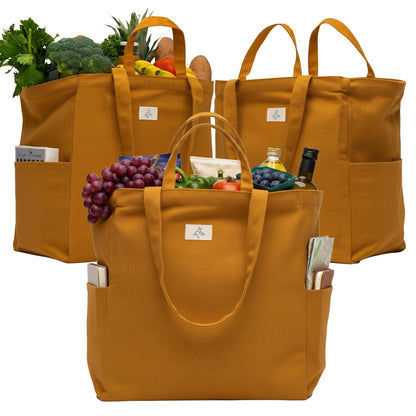 Three mustard yellow Nook theory cotton canvas grocery bags filled with groceries on a white background