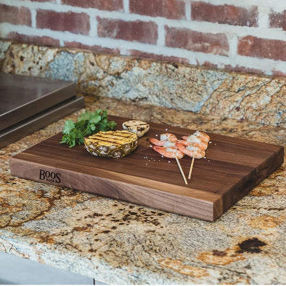 Wooden cutting board with grilled pineapple and shrimp skewers on a granite countertop.