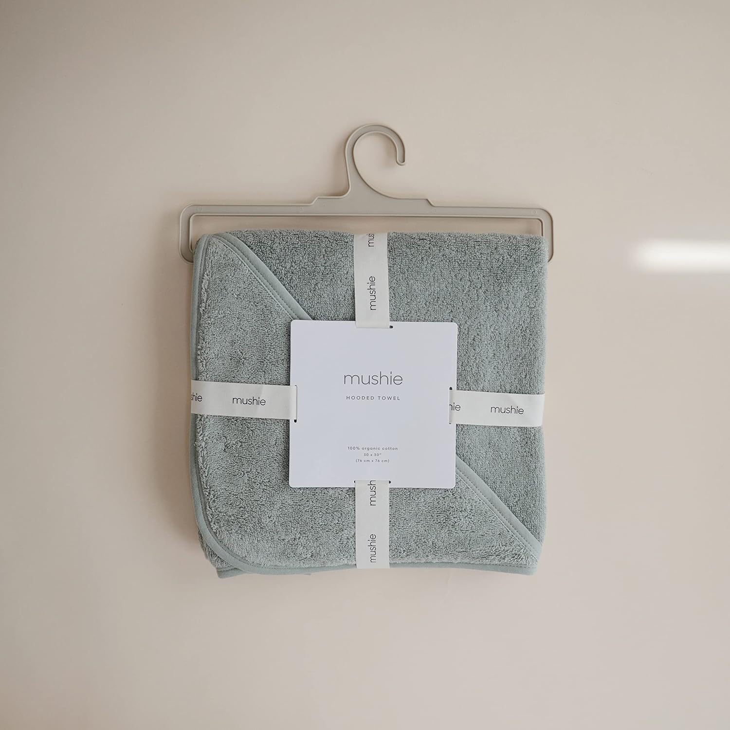 Folded towel with 'mushie' label on a beige hanger against a beige wall