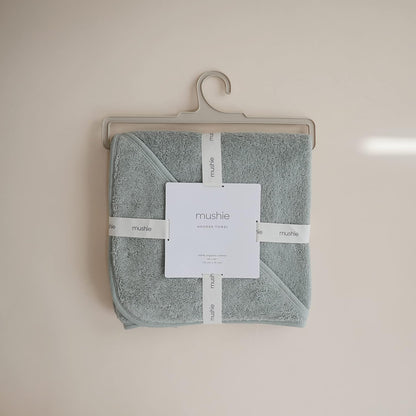 Folded towel with 'mushie' label on a beige hanger against a beige wall