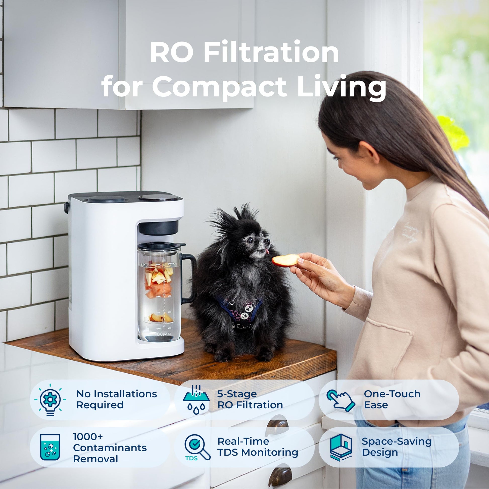 Woman feeding a small dog next to an RO filtration system in a kitchen.