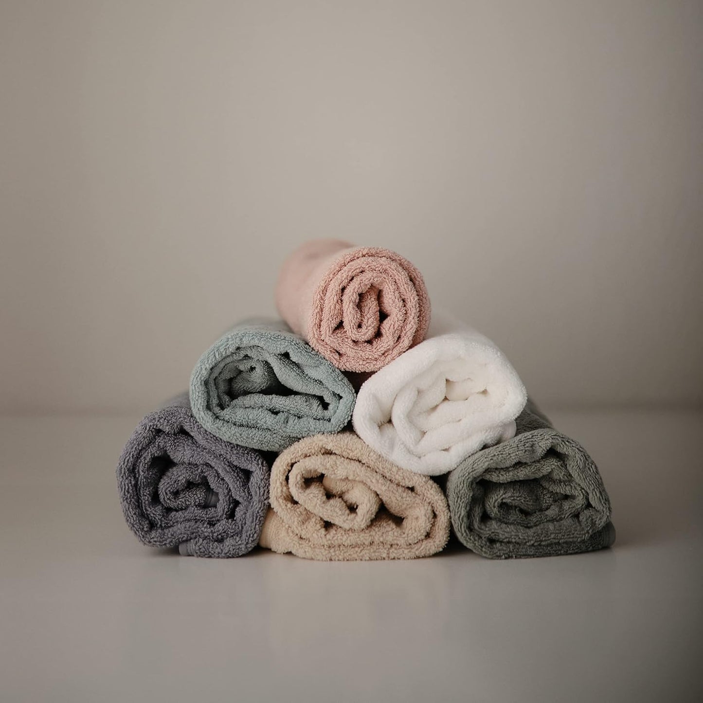 Stack of rolled-up towels in pastel colors on a neutral background