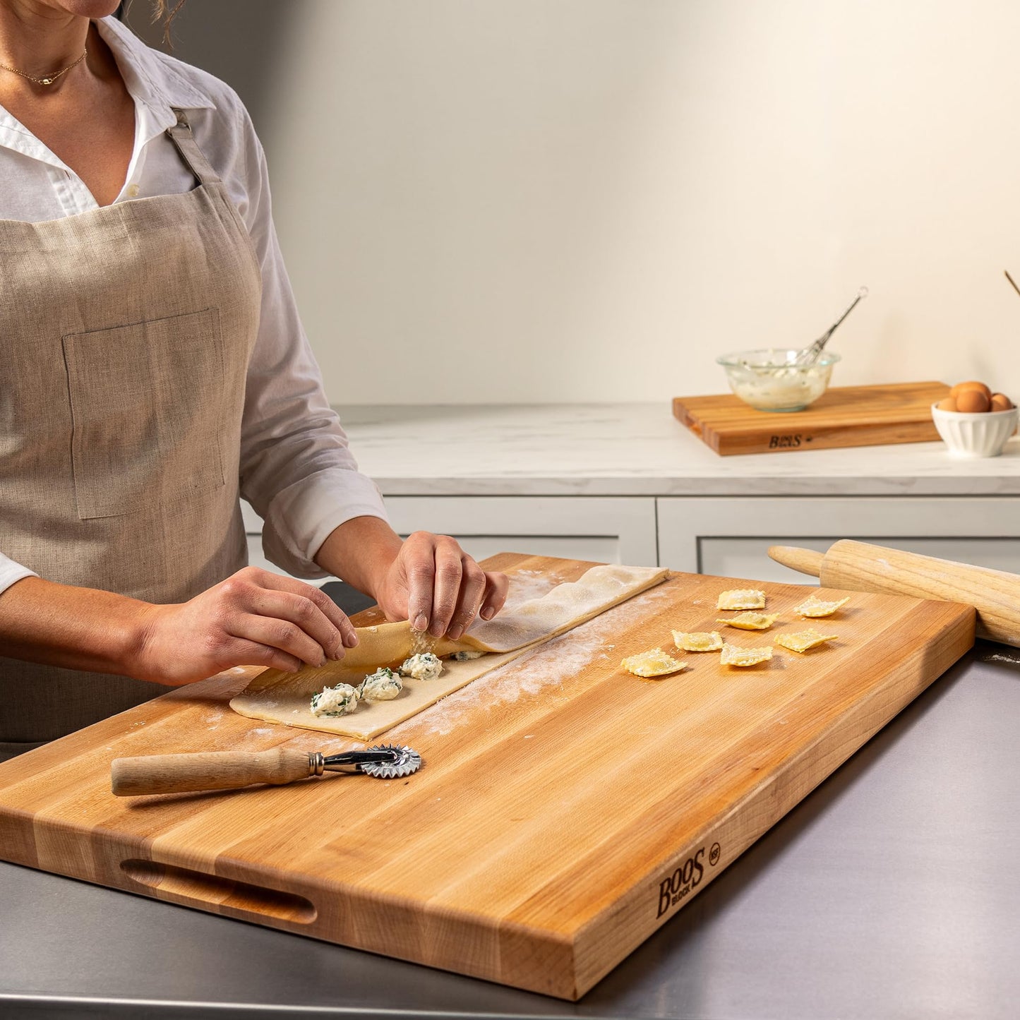 Person in a kitchen preparing food on a wooden cutting board with a rolling pin and other kitchen tools.
