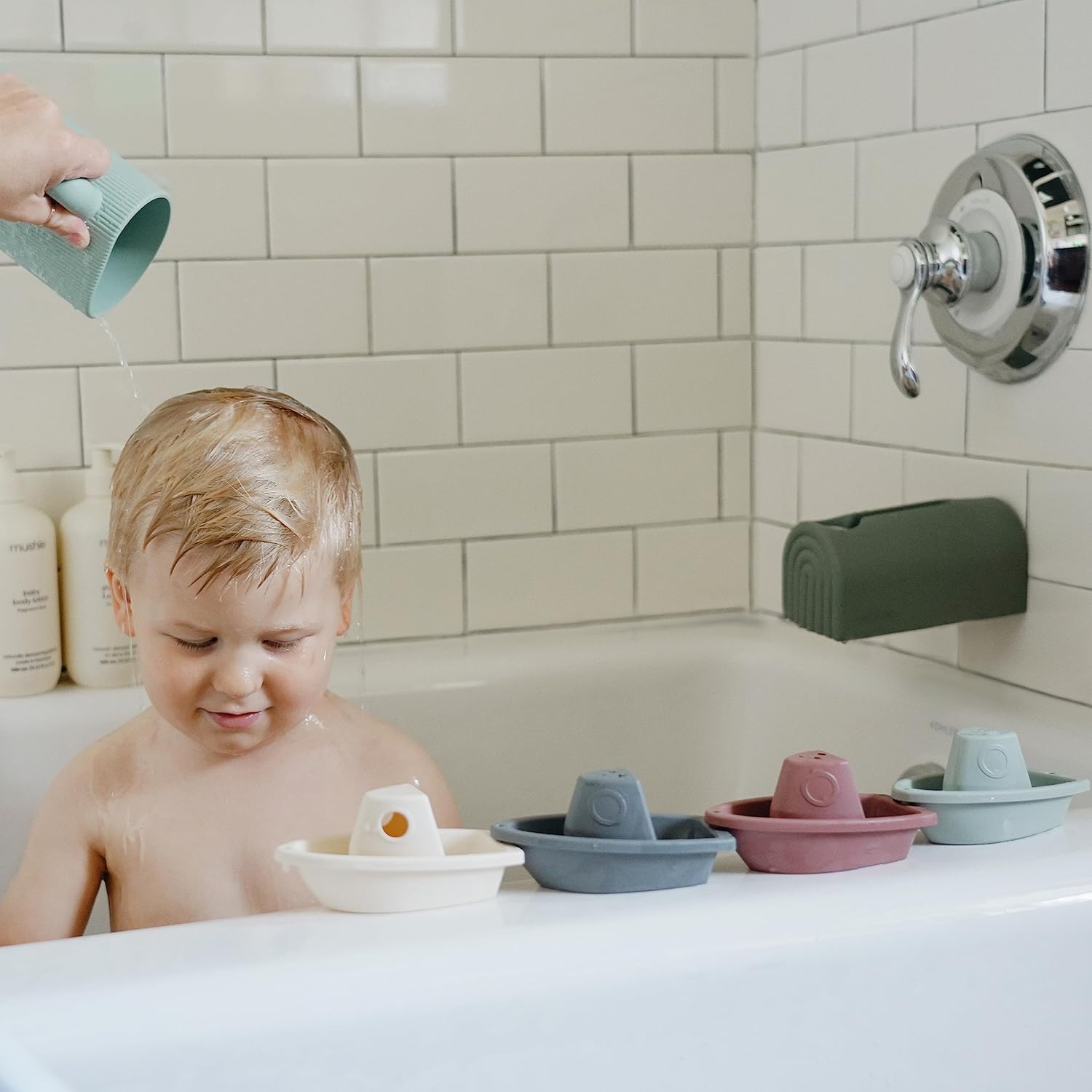 Child playing with bath toys in a bathtub, with a tiled bathroom wall in the background.