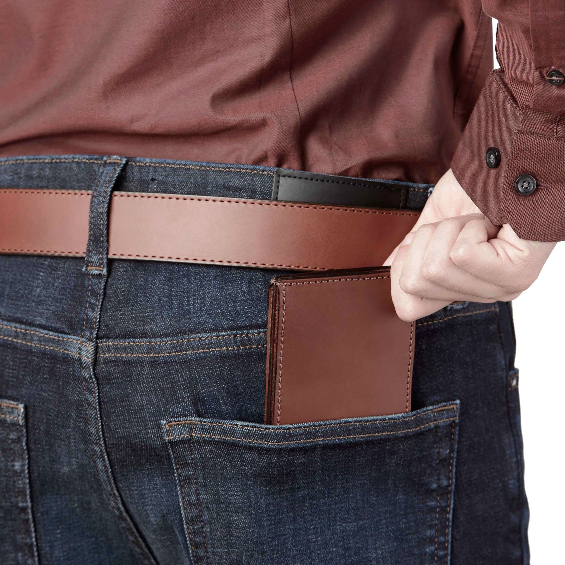 Brown leather wallet in a pocket of blue jeans with a person wearing a brown jacket.