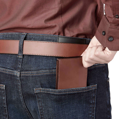 Brown leather wallet in a pocket of blue jeans with a person wearing a brown jacket.