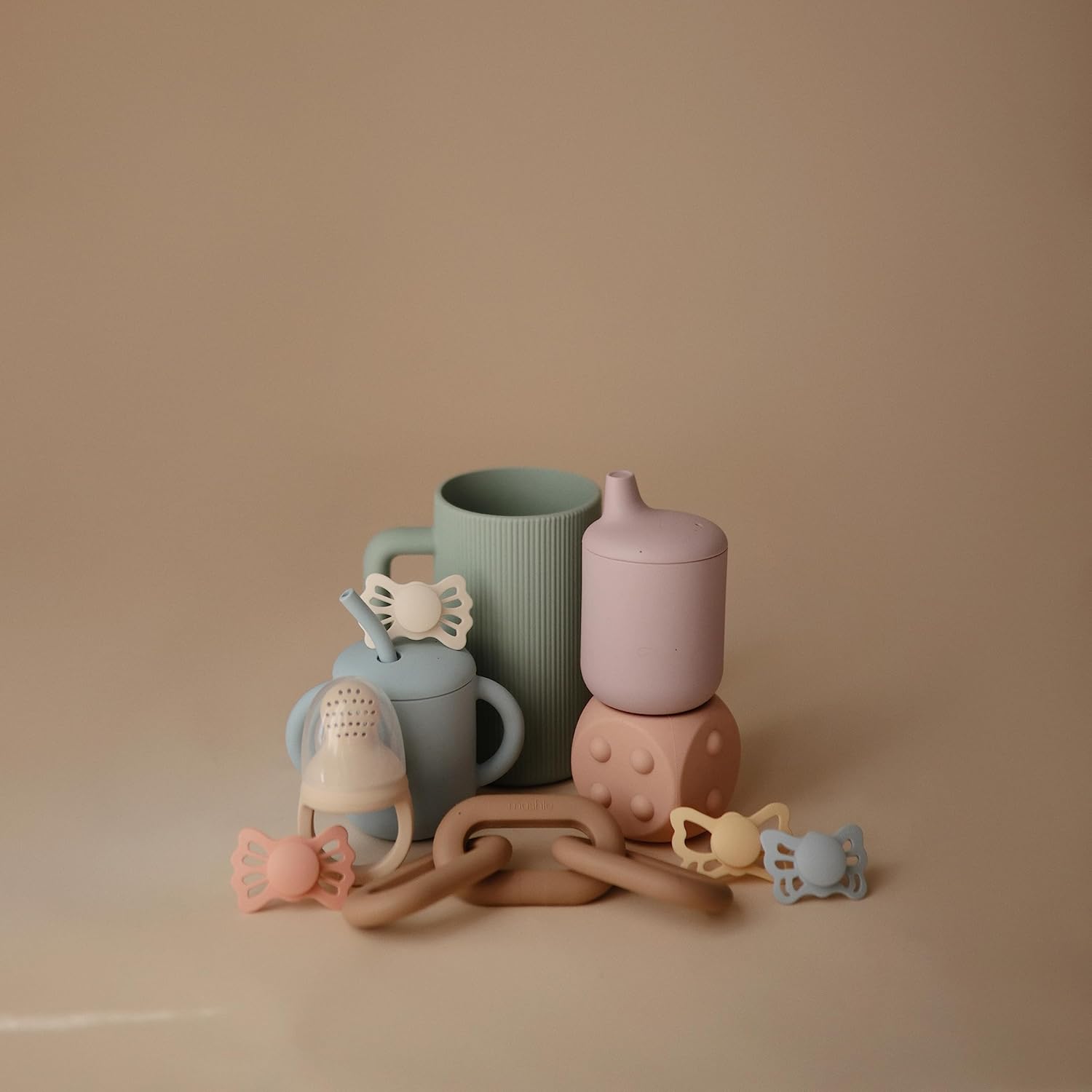 Collection of pastel-colored baby bottles and teething toys on a beige background