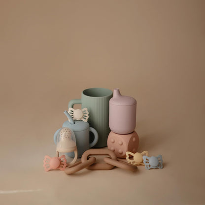 Collection of pastel-colored baby bottles and teething toys on a beige background