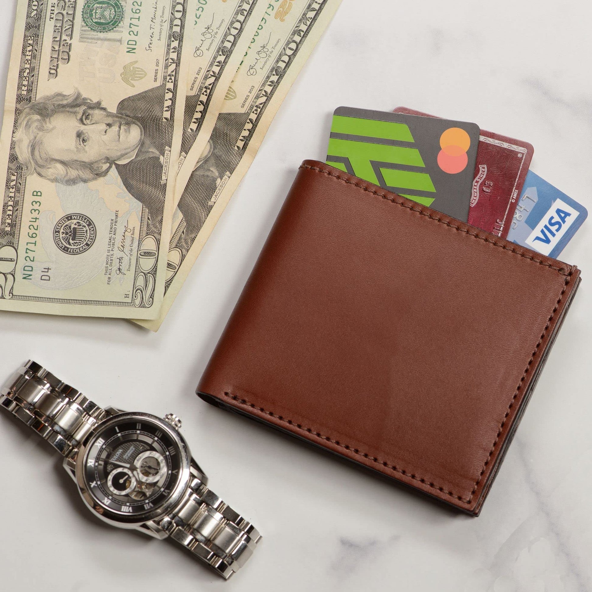 Brown leather wallet with cards, dollar bills, and a watch on a marble surface