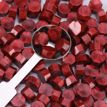 Red hexagonal sealing wax with a metal spoon on a white background