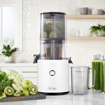 Omega juicer on a kitchen counter with ingredients and a glass of juice.