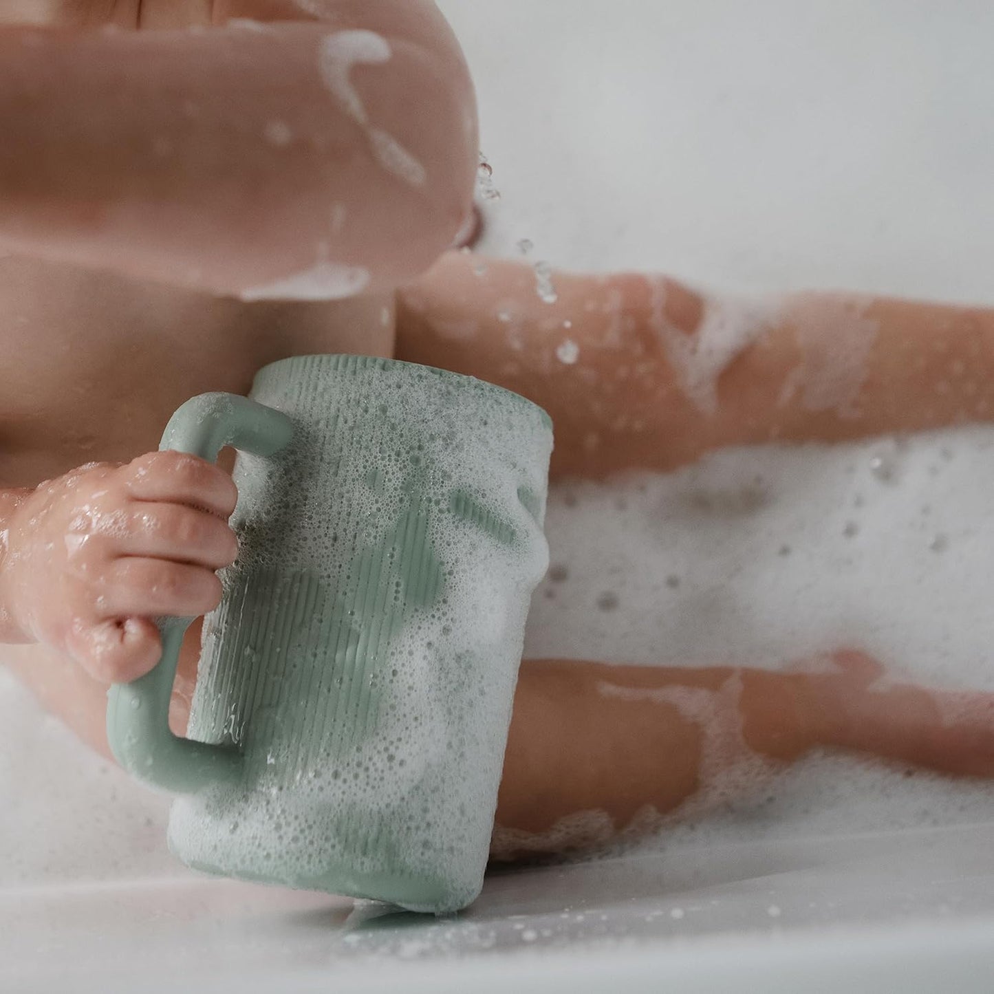 Person holding a green mug in a bathtub filled with bubbles
