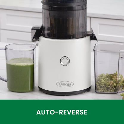 Omega juicer with a glass of green juice and a container of greens on a kitchen counter.