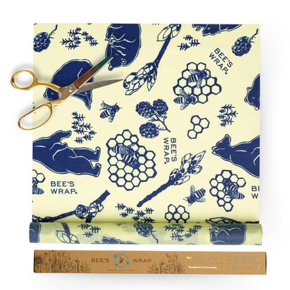 Roll of Bee's Wrap with blue bee and honeycomb pattern on a white background, accompanied by a pair of gold scissors.
