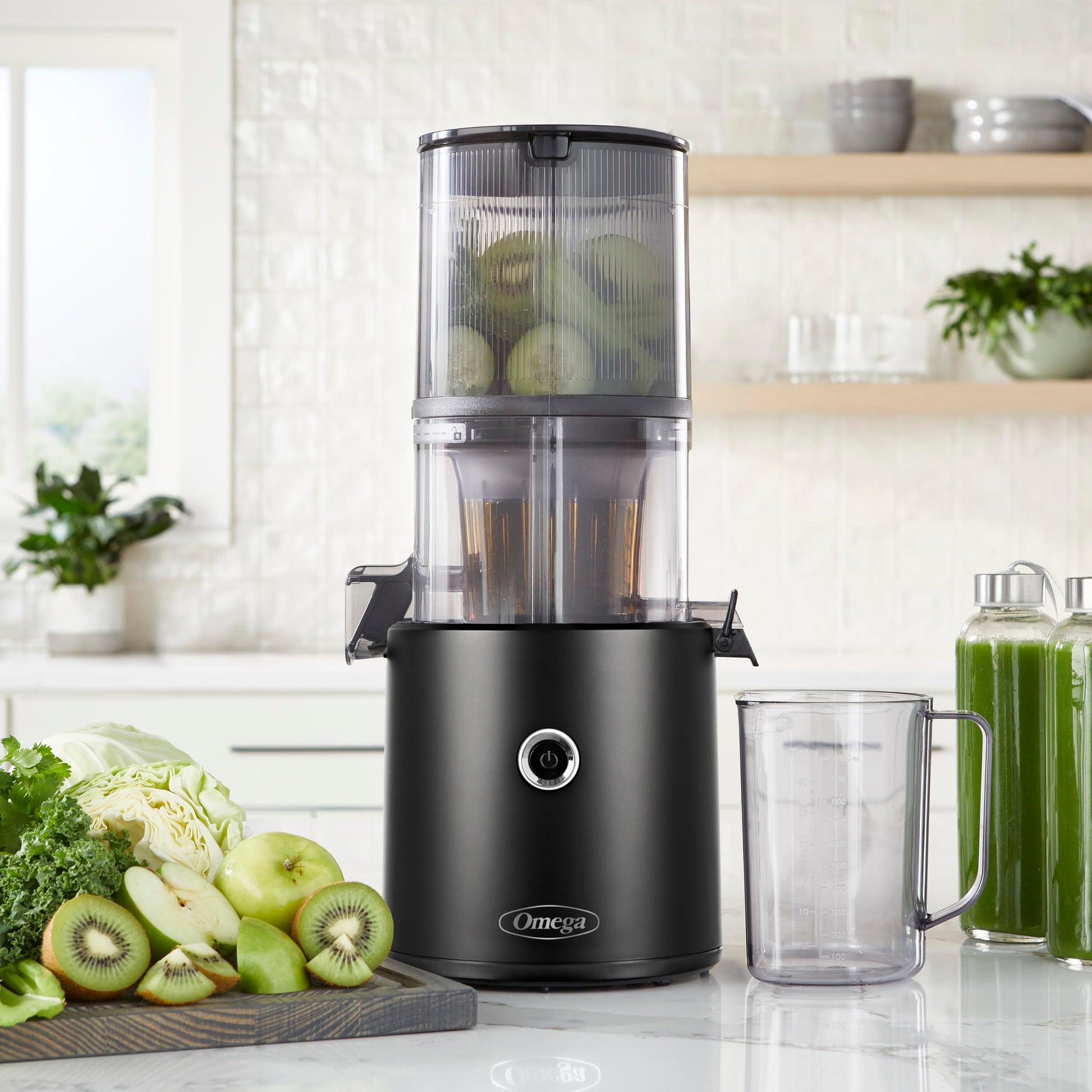 Black Omega juicer on a kitchen counter with ingredients and a glass of juice.