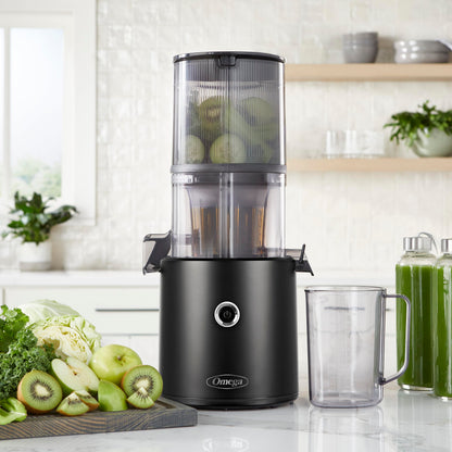 Black Omega juicer on a kitchen counter with ingredients and a glass of juice.