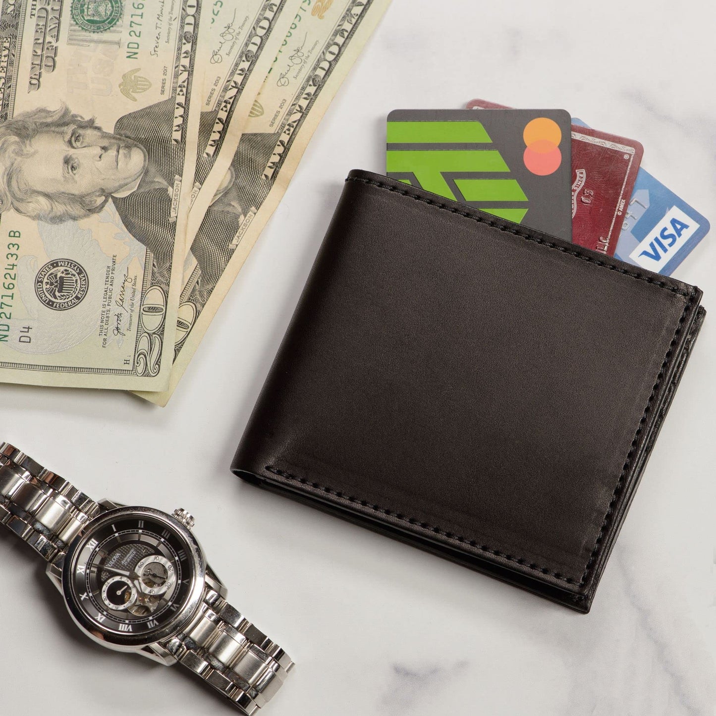 Black wallet with cards, dollar bills, and a watch on a marble surface