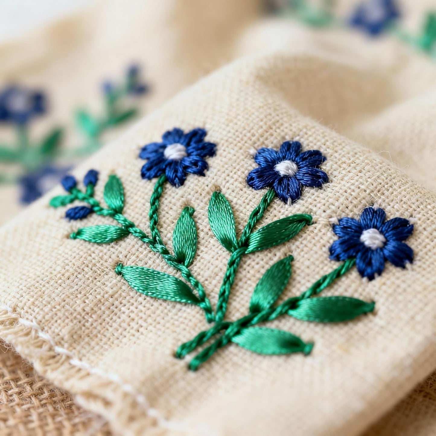 Embroidered blue flowers with green leaves on beige fabric