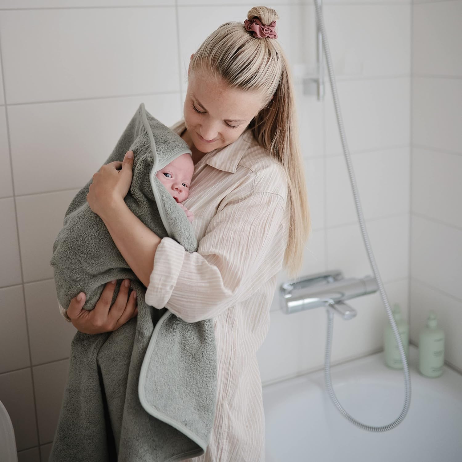 Woman holding a baby wrapped in a towel in a bathroom.