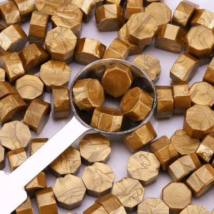 Gold hexagonal sealing wax with a metal scoop on a white background