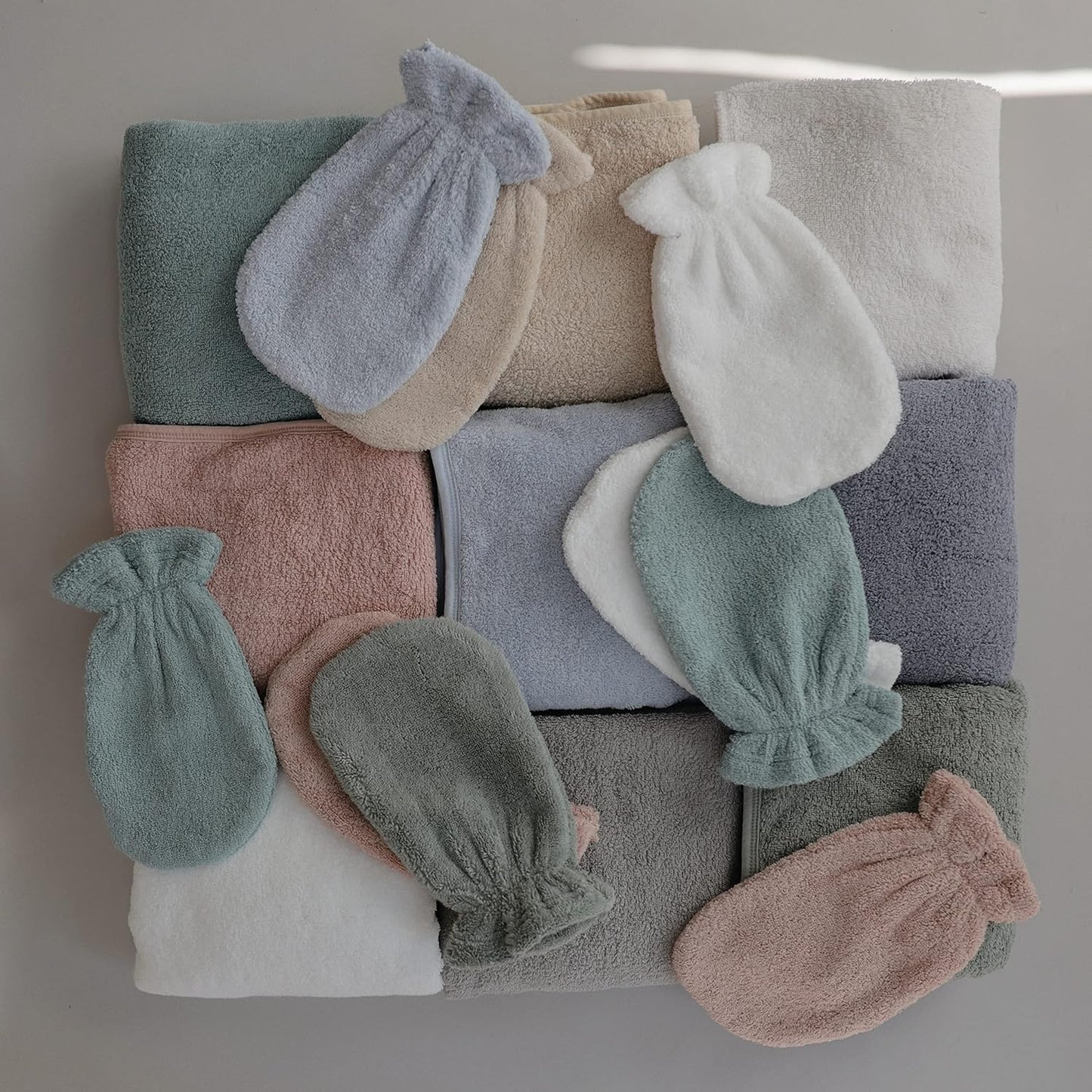 Stack of folded towels and baby booties in various colors on a neutral background