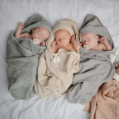 Three newborn babies wrapped in hooded towels on a light gray background