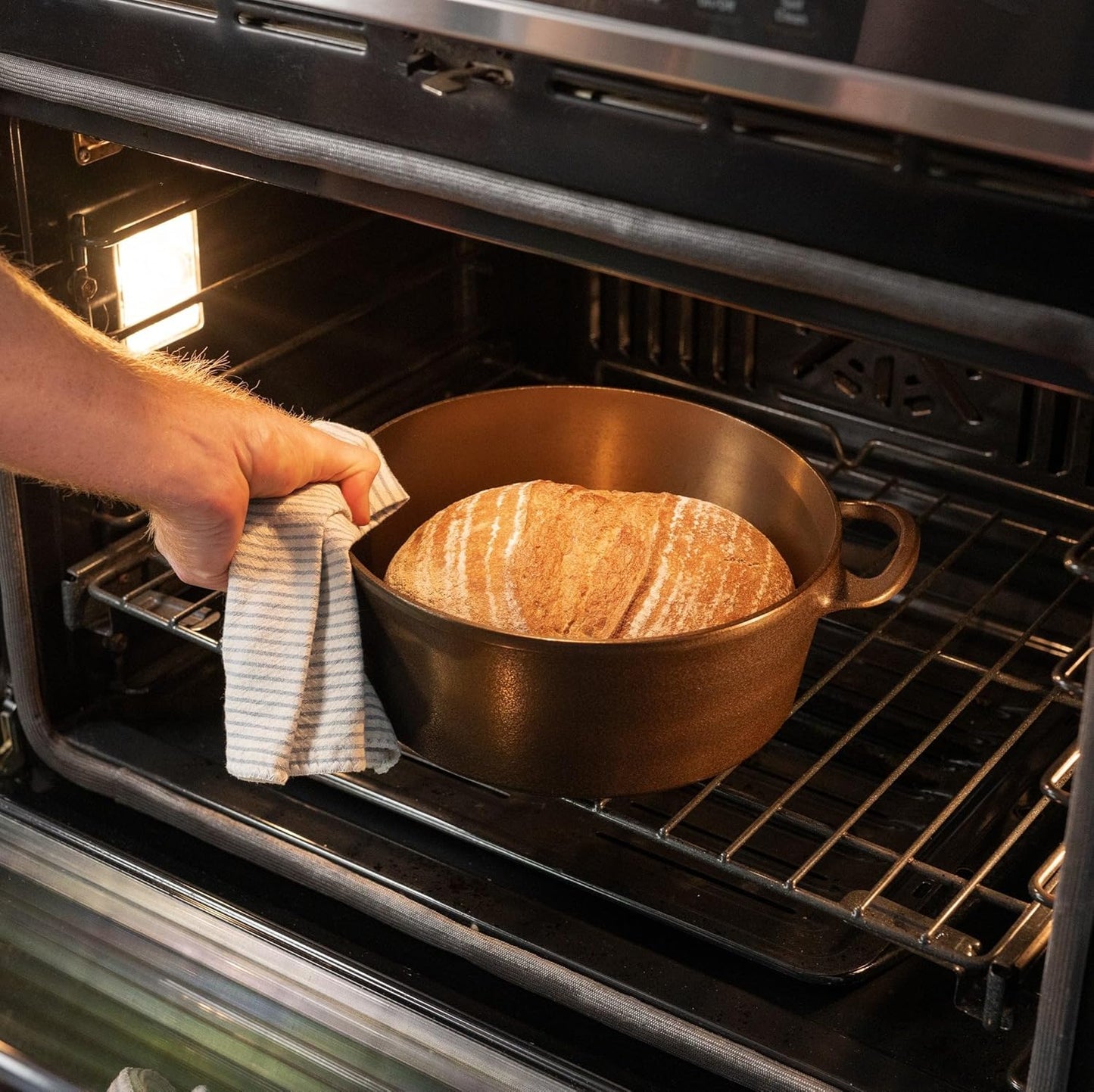 Person placing a pot of bread into an oven using a towel.