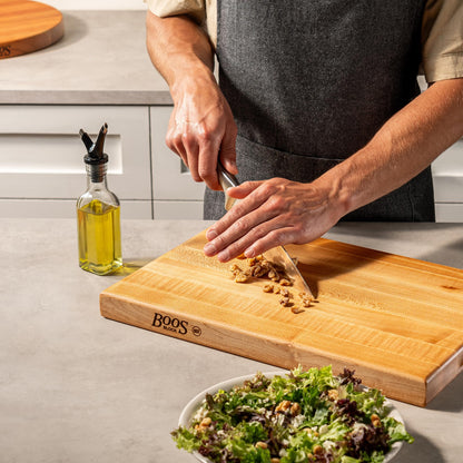 Person preparing a salad on a wooden cutting board with a Boos brand logo.
