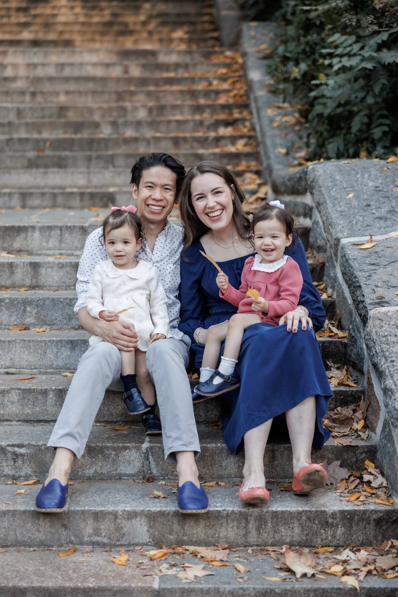 Two women and two children sitting on steps with autumn leaves.